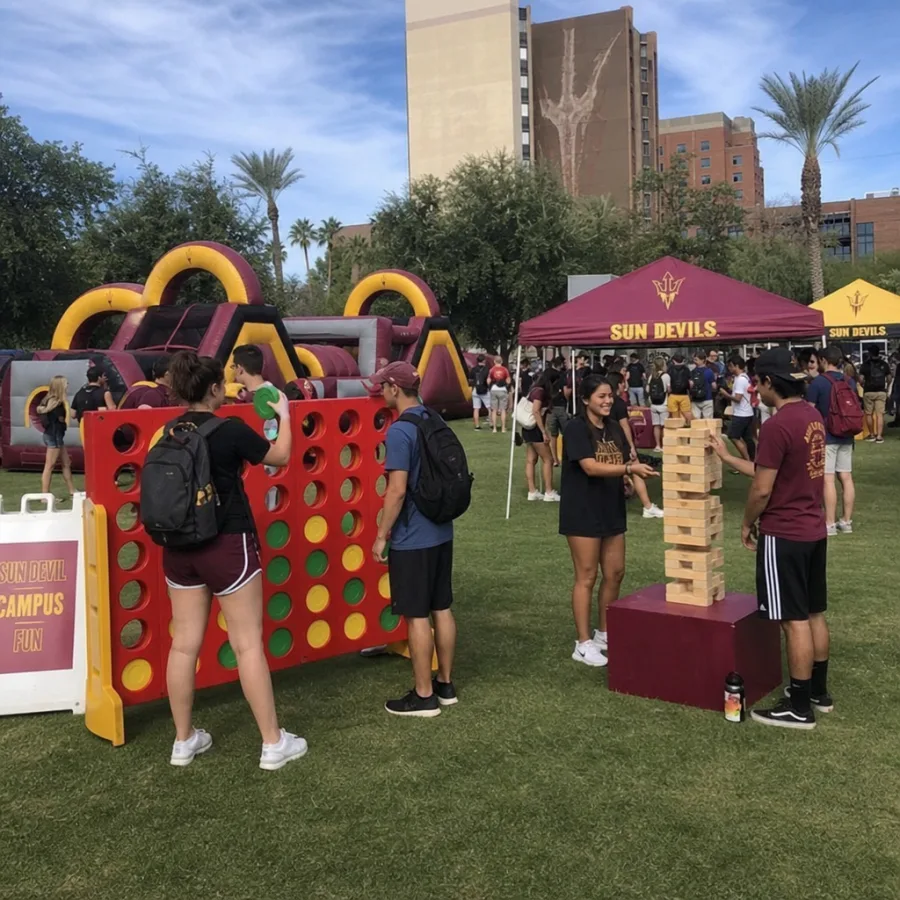 College students playing giant carnival games beside an inflatable obstacle course on a Phoenix campus lawn with shade tents