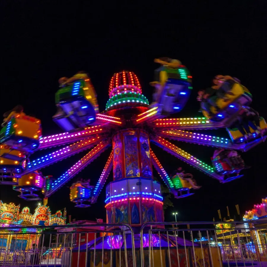 Illuminated carnival ride spinning at night with bright, colorful LED lights against the dark sky