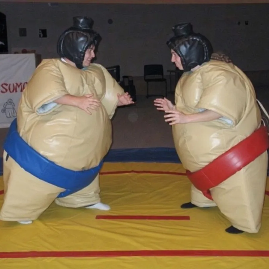 Two friends wearing foam padded sumo wrestling suits and protective headgear facing off in a ring
