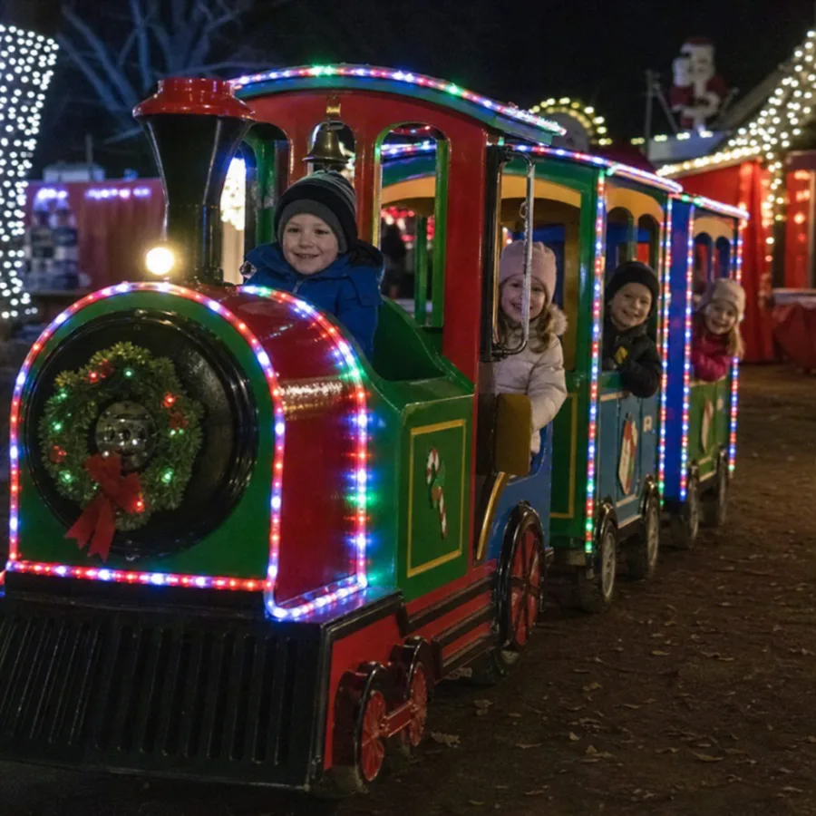 children riding an electric holiday train with festive lights