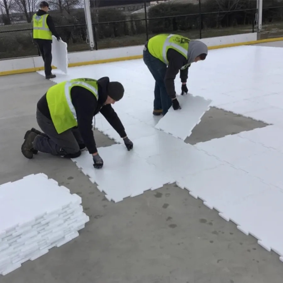 Workers installing interlocking synthetic ice panels over a flat concrete surface