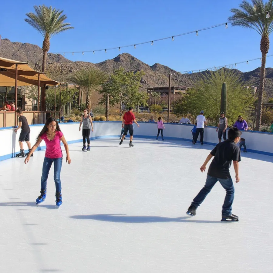 People ice skating on a synthetic polymer rink in a sunny outdoor desert setting